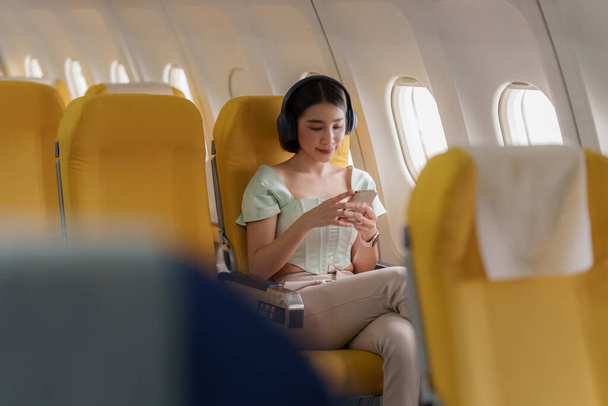 機内飛行中にWi-Fiインターネットに接続されたスマートフォンを使用している若いアジアの女性。旅行のコンセプト. - 写真・画像