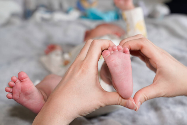 Pies niño del bebé recién nacido en manos de la madre en concepto de familia abrazo piernas del bebé cuerpo en el hogar - Foto, imagen