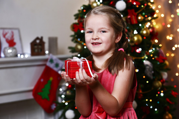 Little girl holding present box near Christmas tree on light background - Photo, Image