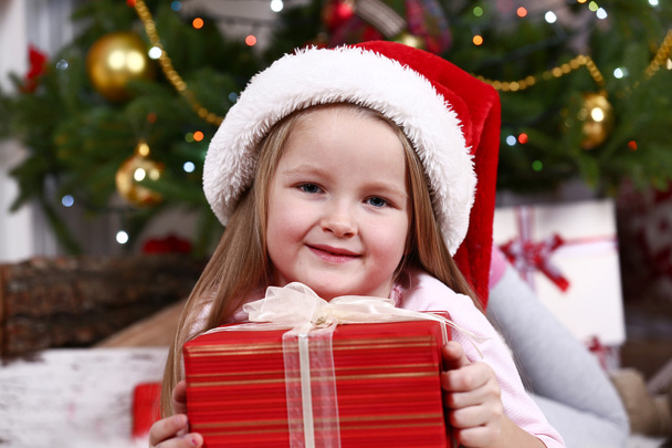Little girl in Santa hat lying on fur carpet on Christmas tree background - Fotoğraf, Görsel