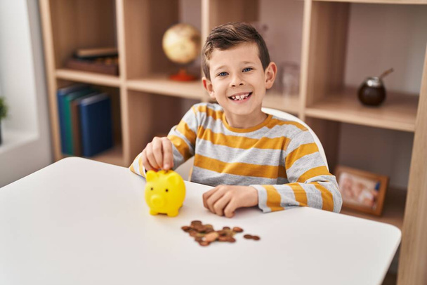 Blond dziecko wkładanie monety na skarbonkę w domu - Zdjęcie, obraz