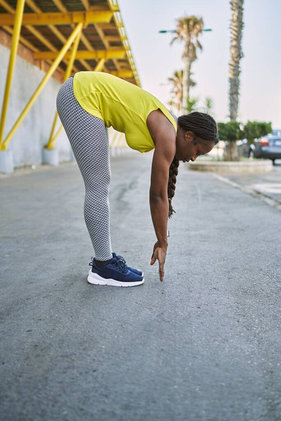 Αφροαμερικανή γυναίκα που φοράει αθλητικά που τεντώνει το πόδι της στο δρόμο - Φωτογραφία, εικόνα