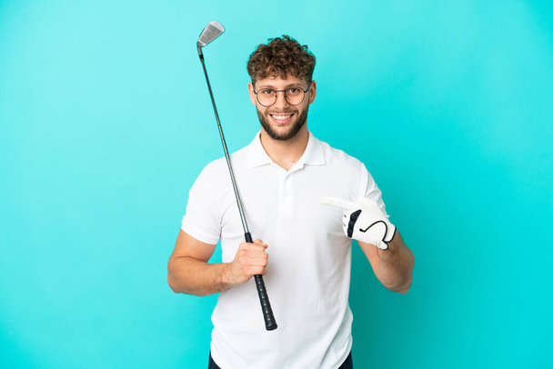 Young handsome caucasian man isolated on blue background playing golf and pointing to the lateral - Foto, Imagen
