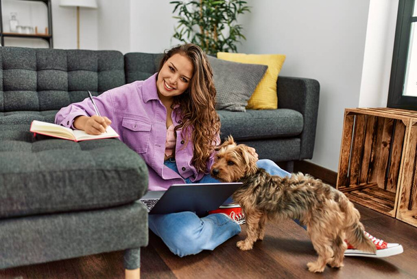 Fiatal gyönyörű spanyol nő használja laptop írás notebook ül a padlón kutyával otthon - Fotó, kép