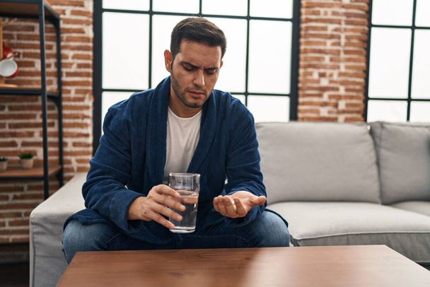 Mladý hispánec bere pilulky sedící doma na pohovce - Fotografie, Obrázek