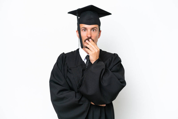 Fiatal egyetemi diplomás férfi elszigetelt fehér háttér meglepett és sokkolt, miközben nézett jobbra - Fotó, kép