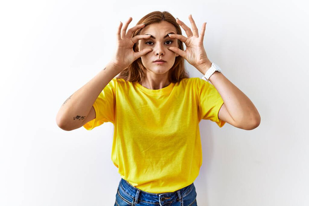 Mladá brunetka žena stojící nad izolovaným pozadím se snaží otevřít oči prsty, ospalý a unavený pro ranní únavu  - Fotografie, Obrázek