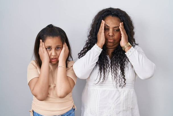 Anne ve küçük kızı beyaz arka planda, elleri başlarının üstünde, stres yüzünden baş ağrısı çekiyorlar. migren ağrısı.  - Fotoğraf, Görsel