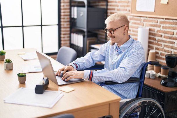 Fiatal fehér férfi üzleti dolgozó ül tolószéken laptoppal az irodában - Fotó, kép