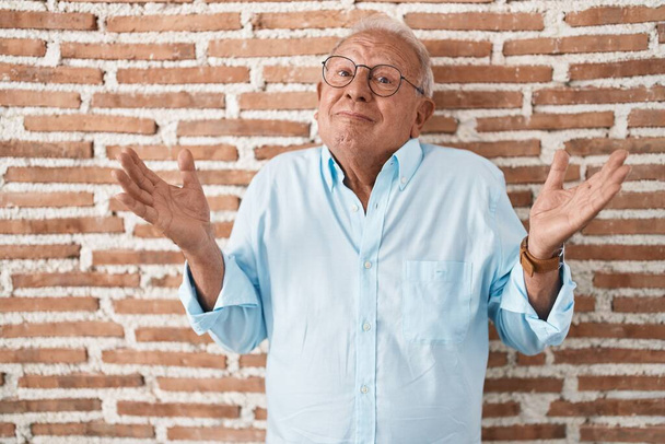 Älterer Mann mit grauen Haaren, der ratlos und verwirrt mit erhobenen Armen und Händen über der Mauer steht. Zweifelhaftes Konzept.  - Foto, Bild