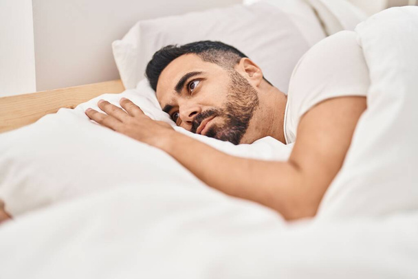 Young hispanic man suffering insomnia lying on bed at bedroom - Фото, зображення