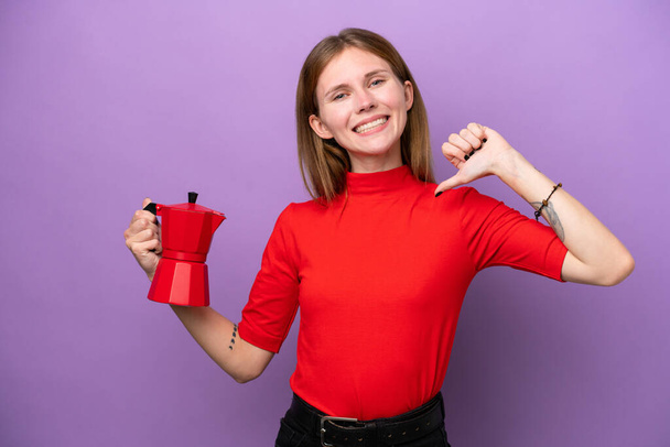 Young English woman holding coffee pot isolated on purple background proud and self-satisfied - Fotoğraf, Görsel