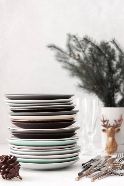 Příprava na slavnostní prostírání stolu, hromada různých talířů a vidliček s noži, jedlové větve v betonové váze, vánoční ozdoby - Fotografie, Obrázek