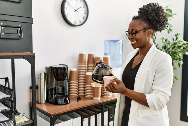 Femme afro-américaine ouvrière versant du café sur la tasse au bureau - Photo, image