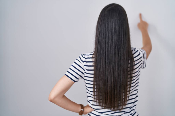 jong brunette vrouw dragen gestreept t shirt poseren achteruit wijzen vooruit met vinger hand  - Foto, afbeelding