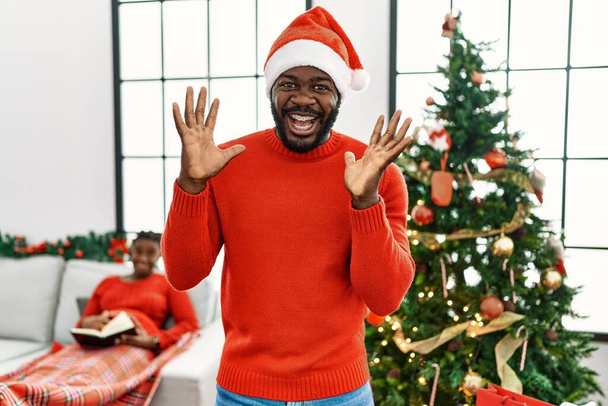 Fiatal afro-amerikai férfi áll a karácsonyfa ünnepli őrült és csodálkozott a siker felemelt karokkal és nyitott szemmel sikoltozó izgatott. győztes koncepció  - Fotó, kép