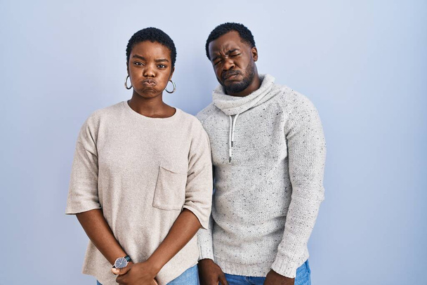 Young african american couple standing over blue background together puffing cheeks with funny face. mouth inflated with air, crazy expression.  - Photo, Image