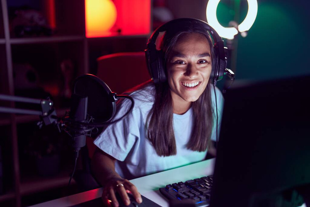Young beautiful hispanic woman streamer playing video game using computer at gaming room - 写真・画像