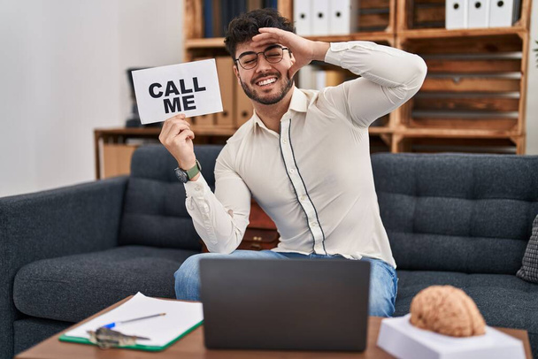 Hispanic man with beard working at therapy office holding call me sign stressed and frustrated with hand on head, surprised and angry face  - Photo, Image