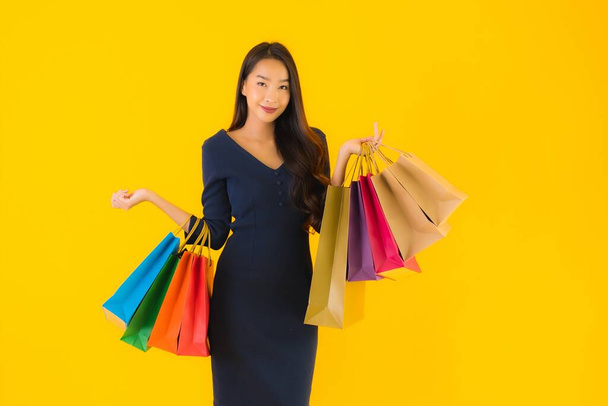 Portrait beautiful young asian woman with colorful shopping bag on yellow isolated background - Photo, Image
