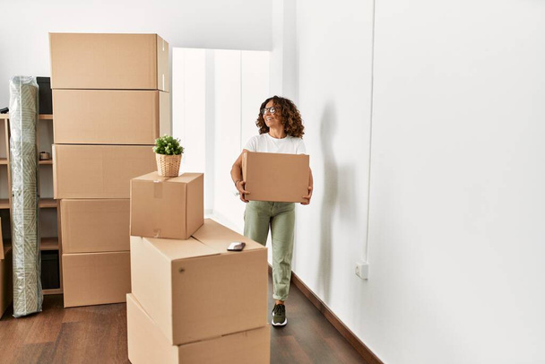 Middle age hispanic woman smiling confident holding cardboard box at new home - Foto, Bild