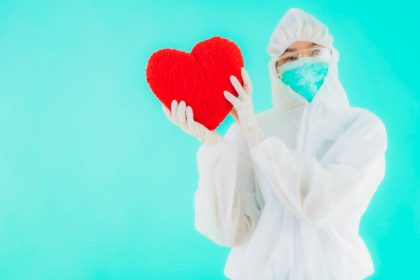 Πορτρέτο όμορφη νεαρή ασιάτισσα γιατρός γυναίκα φορούν ppe ή προσωπικό προστατευτικό εξοπλισμό για την προστασία από coronavirus ή covid19 δείχνουν καρδιά σε μπλε απομονωμένο φόντο - Φωτογραφία, εικόνα
