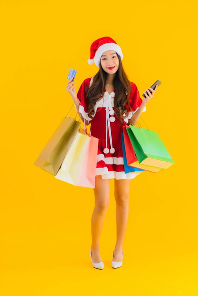 Portret mooie jonge aziatische vrouw dragen kerstmis kleding hoed met veel shopping bag op geel geïsoleerde achtergrond - Foto, afbeelding