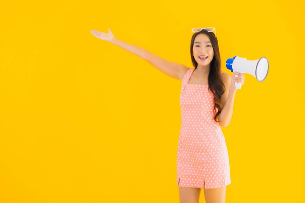 Portrait beautiful young asian woman speak loud with megaphone on yellow isolated background - Фото, зображення