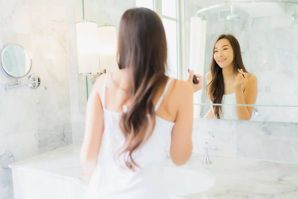 Porträt schöne junge asiatische Frau checken nach oben und Make-up ihr Gesicht auf Spiegel im Badezimmer Interieur - Foto, Bild