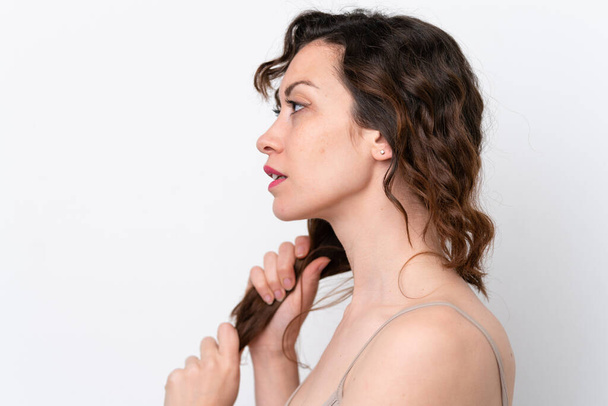 Молодая белая женщина на белом фоне трогает волосы. Портрет крупного плана - Фото, изображение