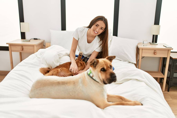 Joven mujer hispana jugando con perros sentados en la cama en el dormitorio - Foto, imagen