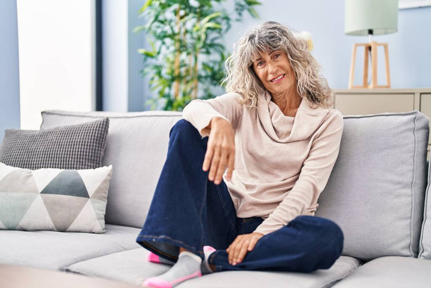 Donna di mezza età sorridente fiducioso seduto sul divano a casa - Foto, immagini