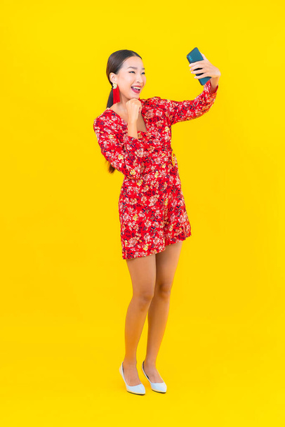 Portrait beautiful young asian woman use smart mobile phone on yellow color background - Fotó, kép