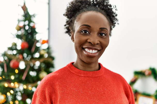 African american woman smiling confident standing by christmas tree at home - 写真・画像