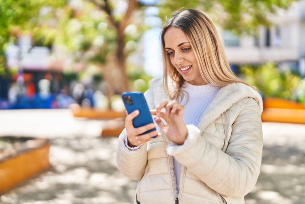 Jonge vrouw lacht vol vertrouwen met smartphone in het park - Foto, afbeelding