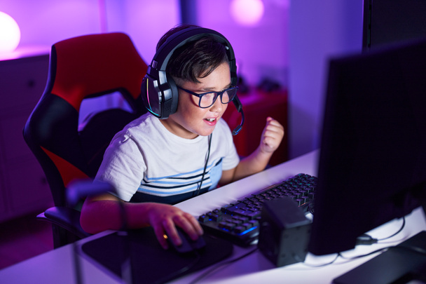 Adorable hispanic boy streamer playing video game with winner expression at gaming room - Zdjęcie, obraz