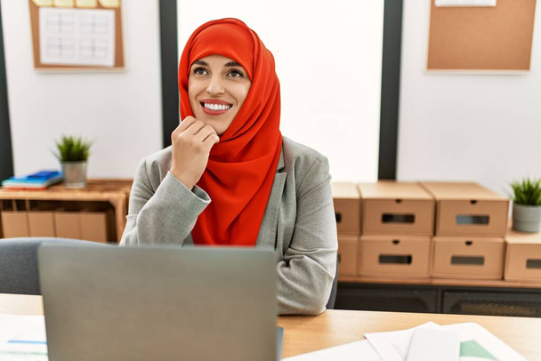 Mujer joven con bufanda árabe usando portátil trabajando en la oficina - Foto, imagen