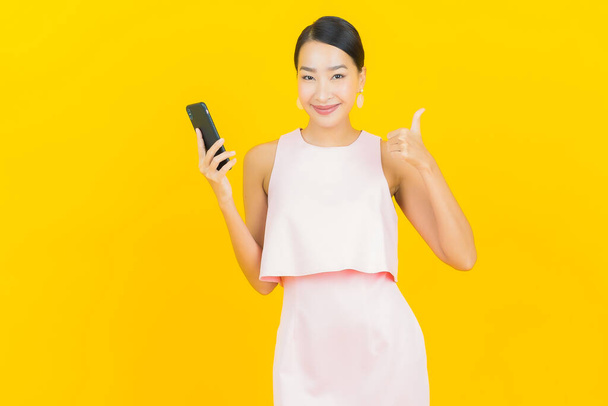 Portrait beautiful young asian woman smile with smart mobile phone on yellow color background - 写真・画像