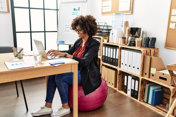 Young african american woman smiling confident working sitting on fit ball at office - Фото, изображение