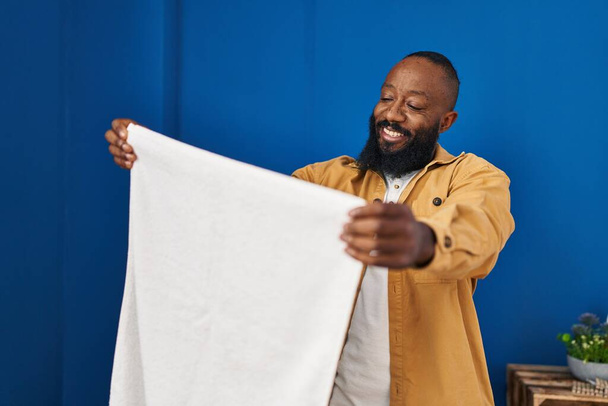 若いアフリカ系アメリカ人の男は洗濯室で自信を持ってタオルを保持笑顔 - 写真・画像