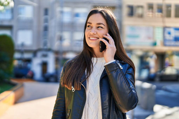 Mujer joven sonriendo confiada hablando en el teléfono inteligente en el parque - Foto, imagen