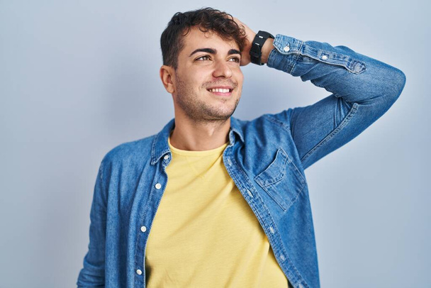 Молодой латиноамериканец, стоящий на синем фоне, уверенно улыбающийся, трогательные волосы с жестом вверх рукой, позируя привлекательным и модным  - Фото, изображение