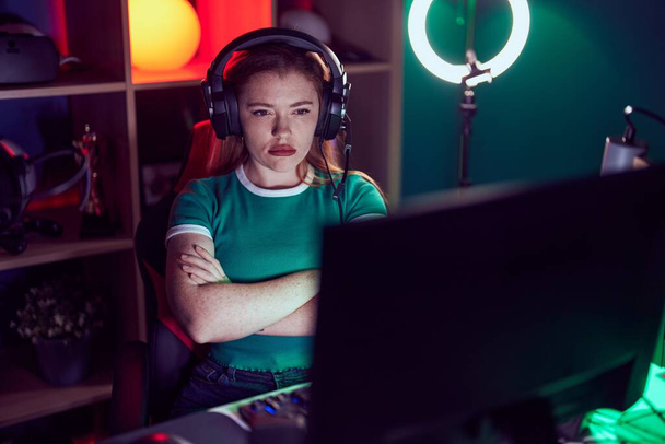 Femme rousse jouant à des jeux vidéo sceptique et nerveux, expression désapprobatrice sur le visage avec les bras croisés. personne négative.  - Photo, image