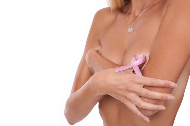 A tanned woman shows a sign of fighting breast cancer by covering her breasts with her hand. Studio photo on white background - Fotografie, Obrázek