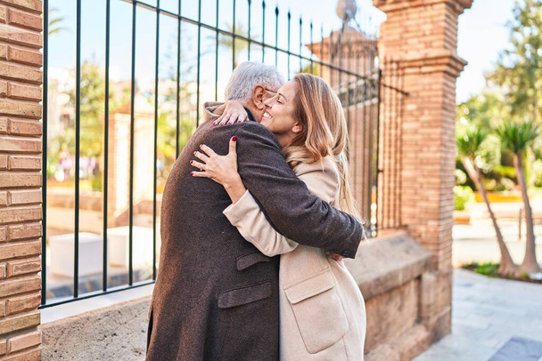 Middelbare leeftijd man en vrouw paar knuffelen elkaar staan op straat - Foto, afbeelding