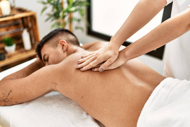 Joven hispano relajado teniendo masaje de espalda en el centro de belleza - Foto, Imagen