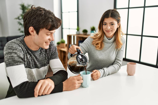 Young caucasian couple having breakfast pouring coffee on cup at home. - Φωτογραφία, εικόνα