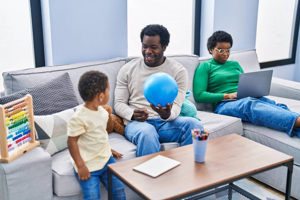 Afroamerikanische Familie spielt mit Ball und benutzt Laptop zu Hause - Foto, Bild