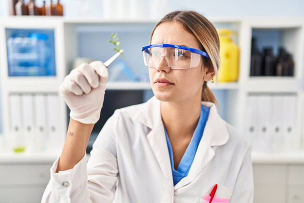 Junge hispanische Wissenschaftlerin hält Pflanzenprobe mit Pinzette im Labor - Foto, Bild