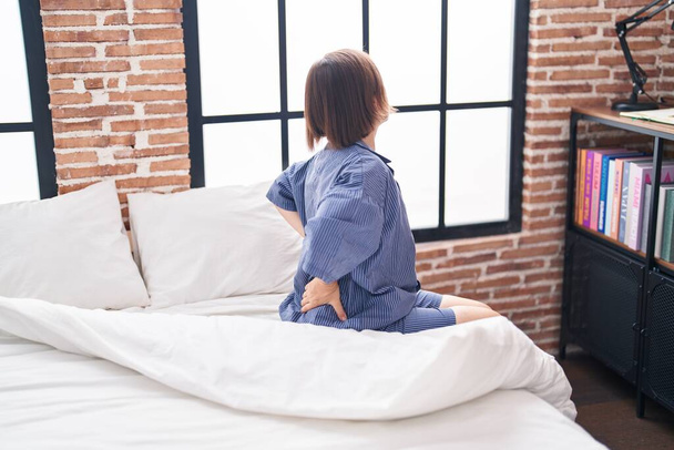 Femme d'âge moyen souffrant d'une blessure au dos assise sur le lit dans la chambre - Photo, image
